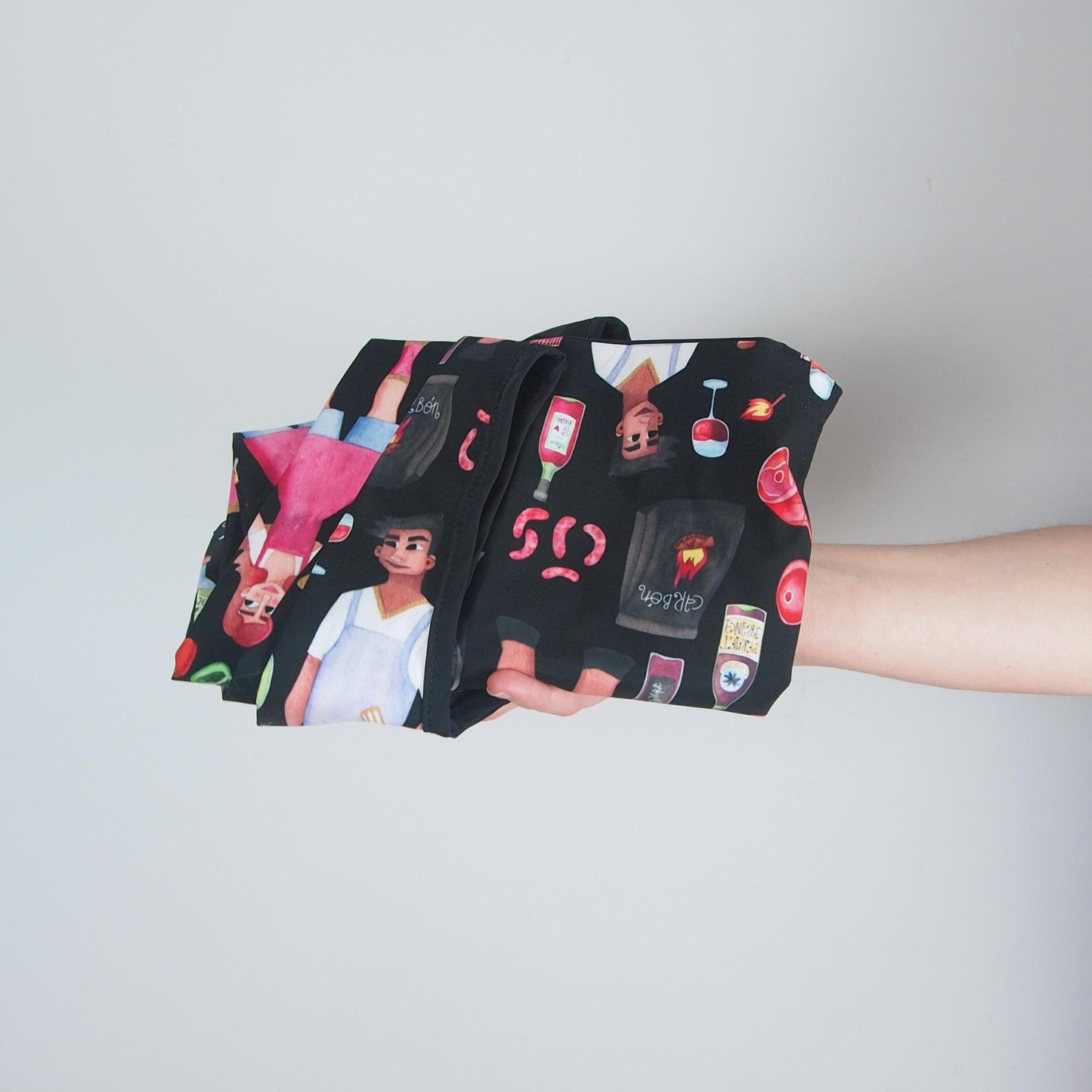 Black fabric with colorful designs held by a person against a light gray background