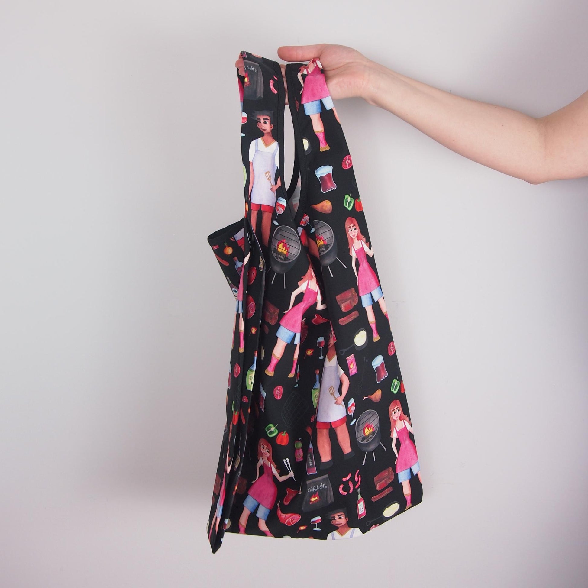 Black apron with colorful graphics held by a hand against a light gray background