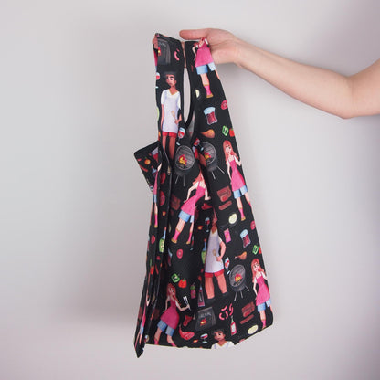 Black apron with colorful graphics held by a hand against a light gray background